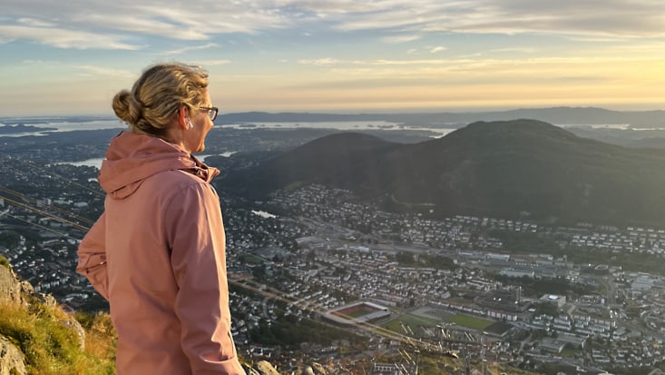 Frau blickt in der Abendsonne von einem Hügel auf eine Stadt im Tal.