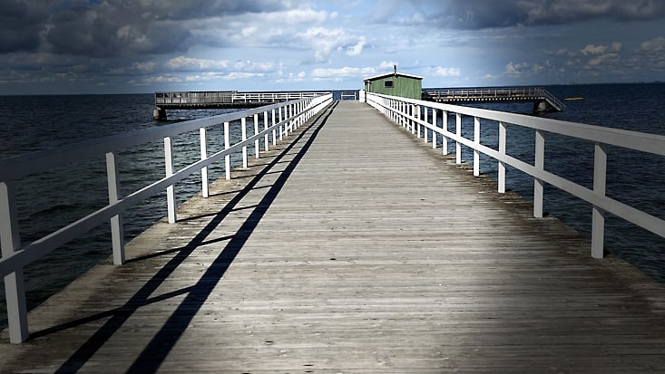 Ein Steg der aufs Meer führt. Zu sehen ist der Steg, ein grünes Häuschen und der Horizont.