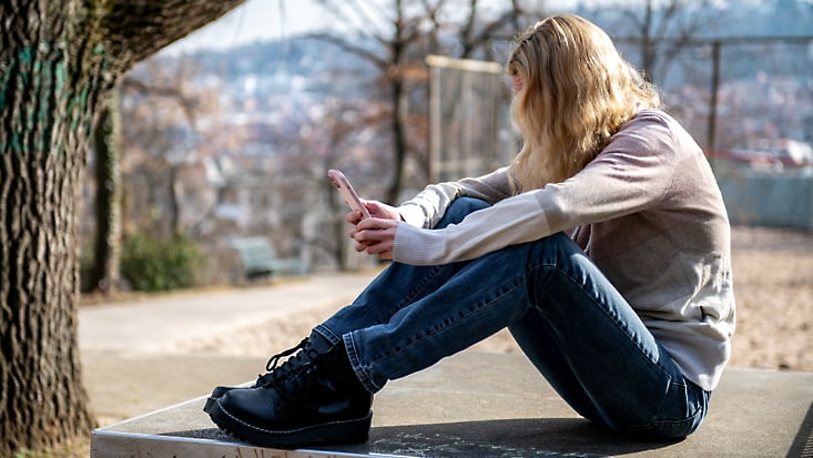 Frau schaut betrübt auf ihr Handy