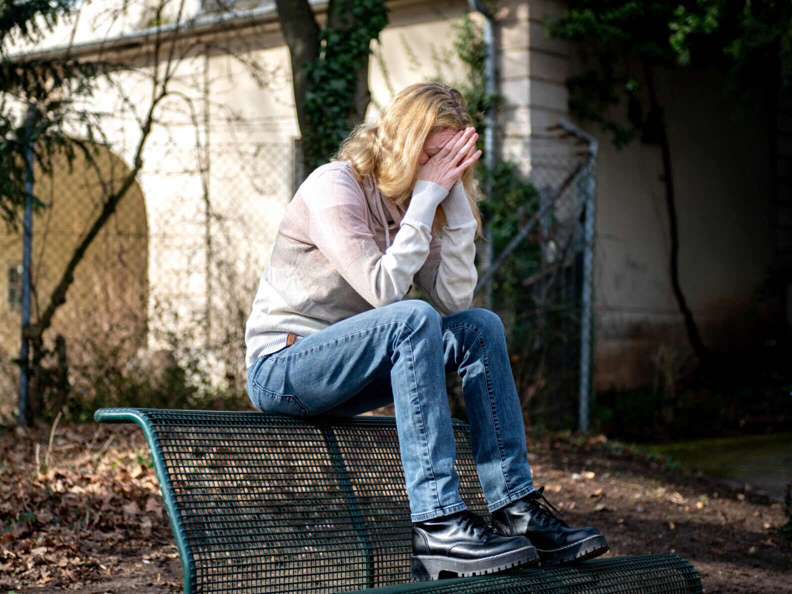 Eine Frau sitzt einsam auf einer Parkbank, hat das Gesicht in ihren Händen vergraben