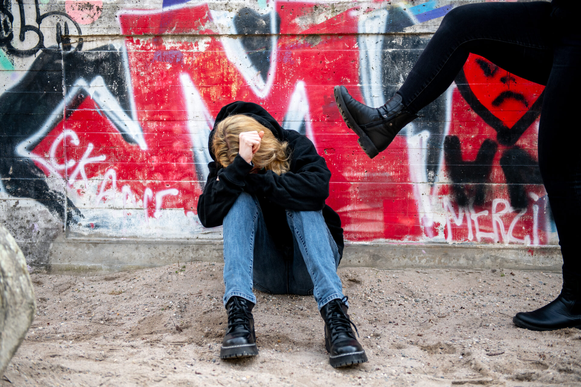Eine am Boden sitzende person wird von einer über ihr stehenden Person missbraucht, indem sie mit dem Fuß auf sie eintritt